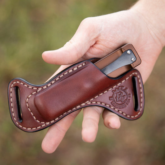 Hand holding a leather knife sheath with a blurred natural background
