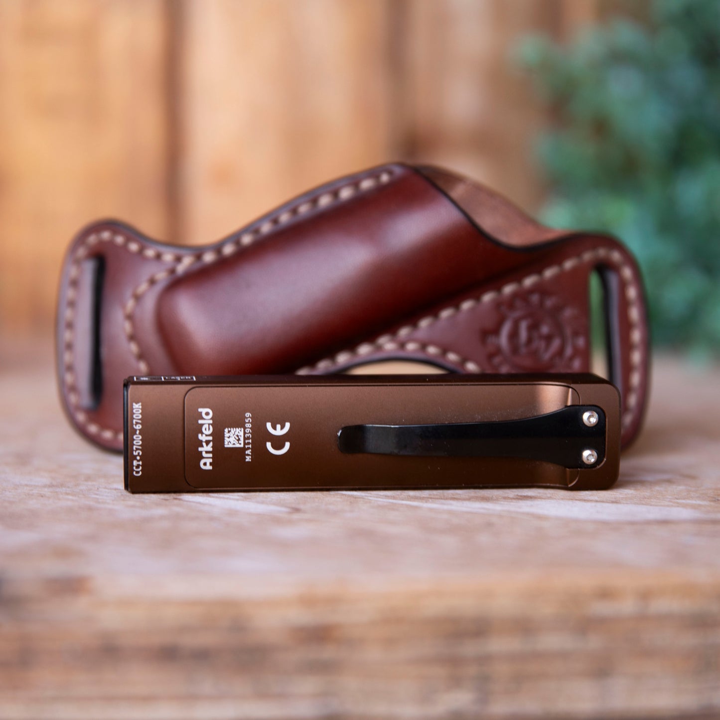 Brown leather case with a metallic desert tan Arkfeld flashlight on a wooden surface