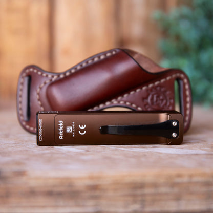 Brown leather case with a metallic desert tan Arkfeld flashlight on a wooden surface