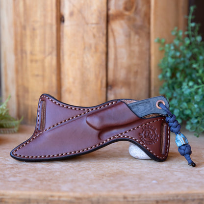 Handmade brown leather scout carry sheath for Benchmade Dacian, shown with knife in sheath on a wooden background.