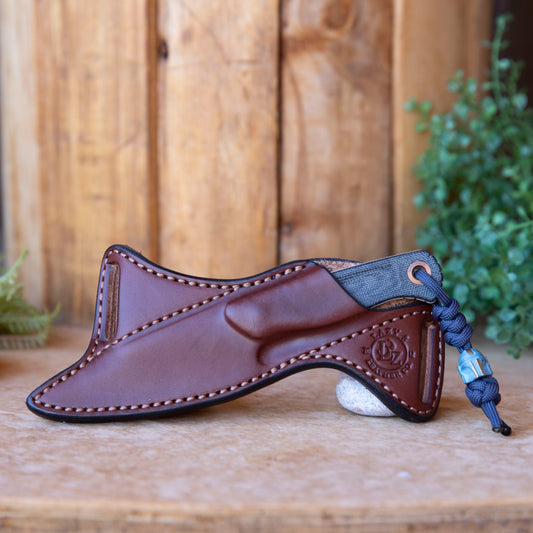 Handmade brown leather scout carry sheath for Benchmade Dacian, shown with knife in sheath on a wooden background.