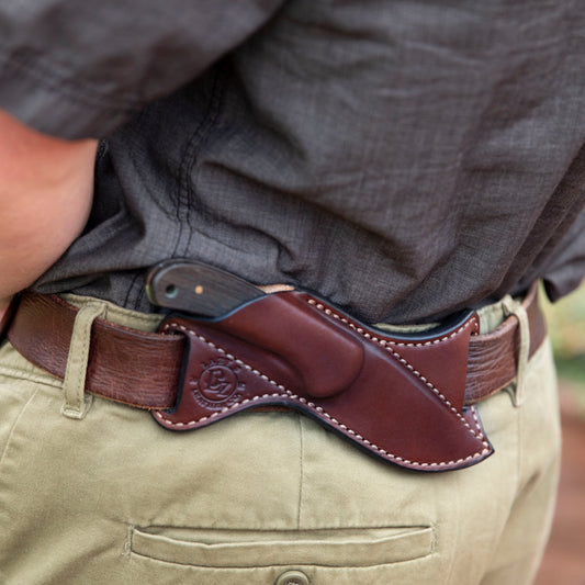 Brown leather knife sheath on a person's belt with a Ranger Skinner Buck 113 knife in the sheath.