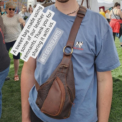 Person wearing a blue t-shirt with a brand logo and carrying a brown leather bag made from our scrap box at an outdoor event.