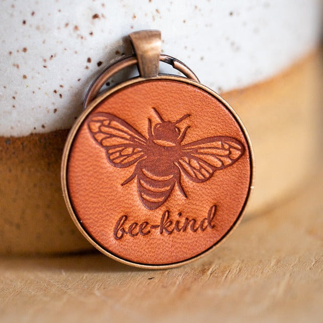 Stamped leather pendant keychain with a honey bee on it and the words bee-kind. This keychain is made using Vegetable tanned leather from Wickett & Craig.